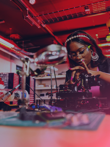 Ung kvinna med långa naglar löder ihop ett kretskort.