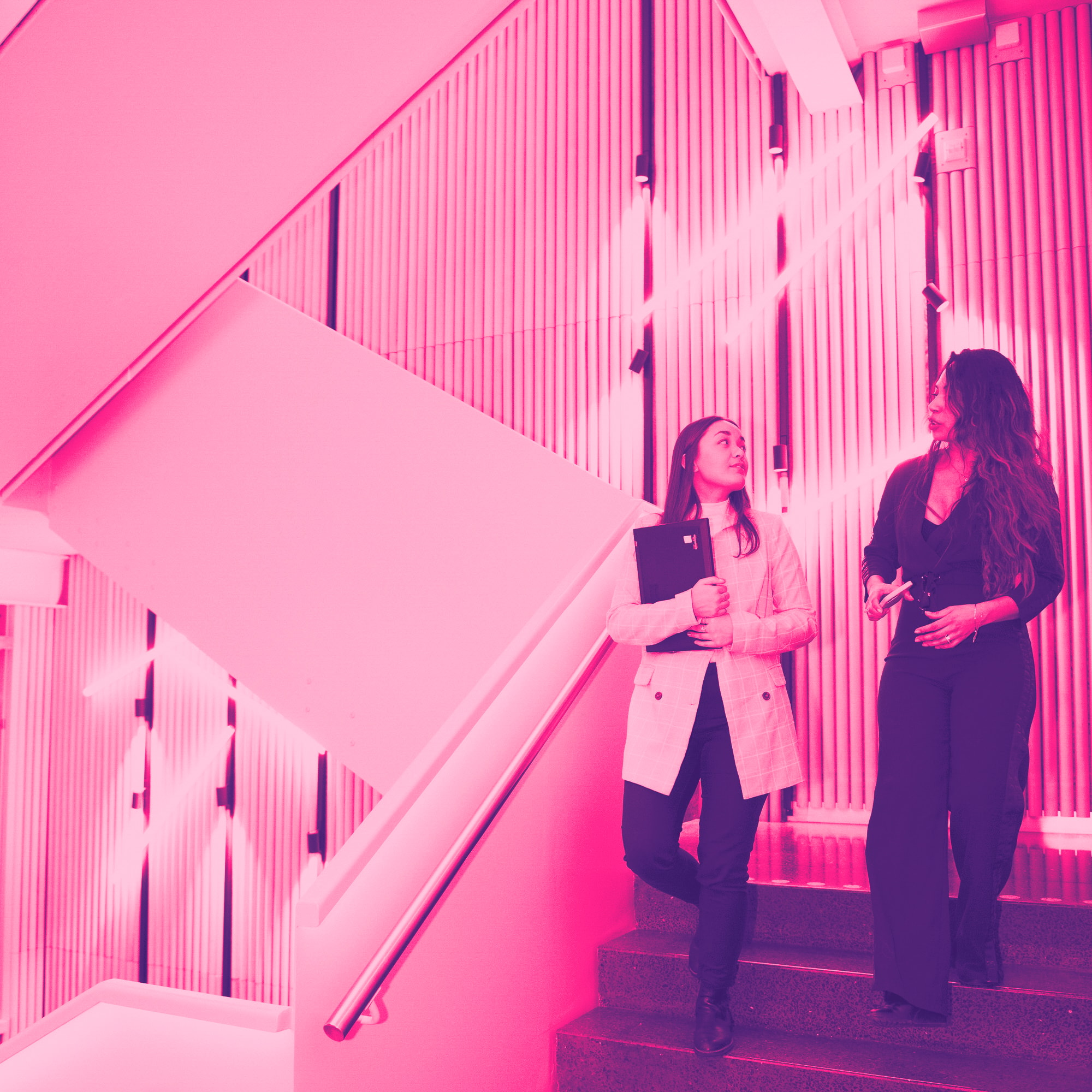 Två kvinnor som diskuterar på väg ner för en trappa. Med rosa filter