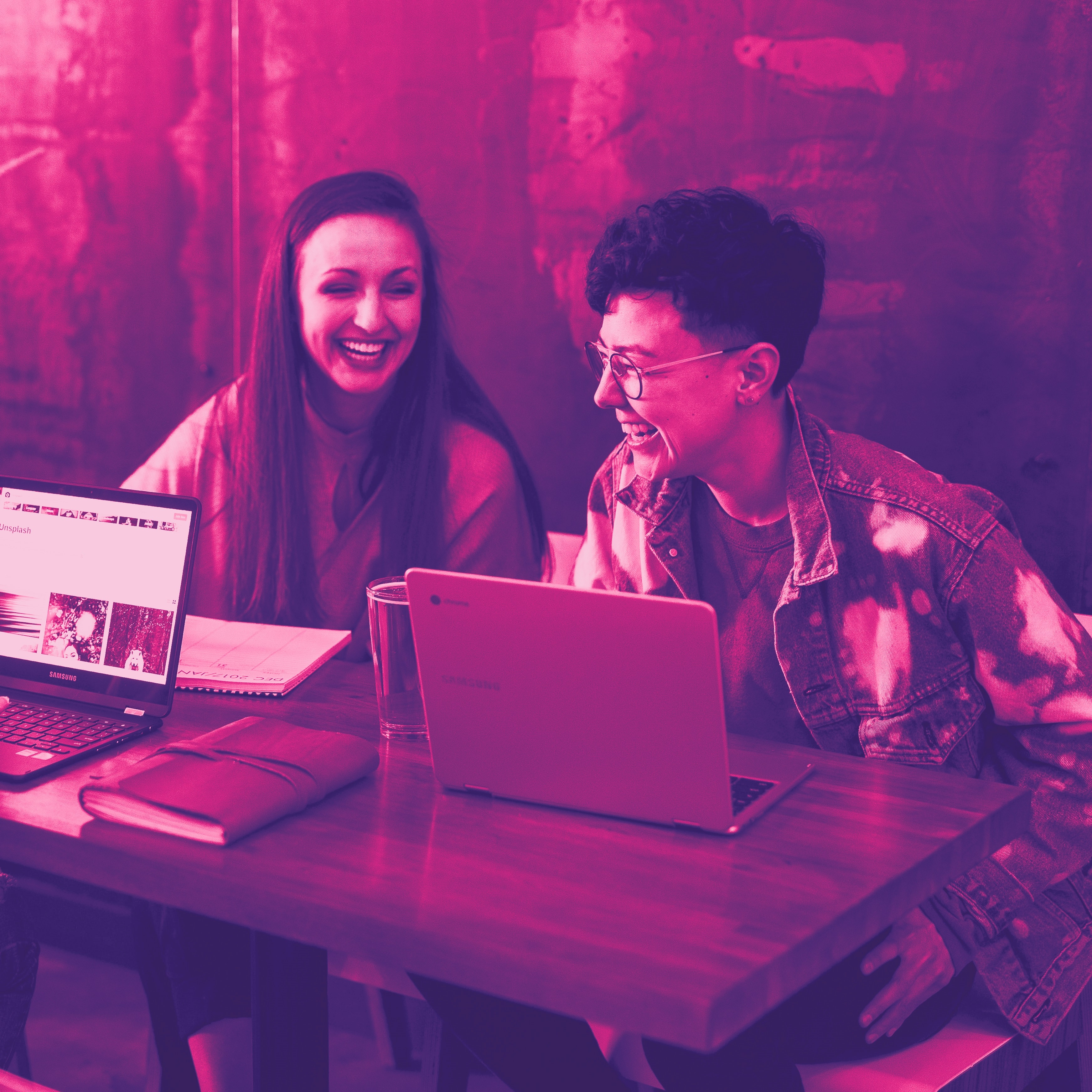 Tre kvinnor sitter vid en arbetsplats med datorer och skrattar, skämtar med varandra. Med rosa filter