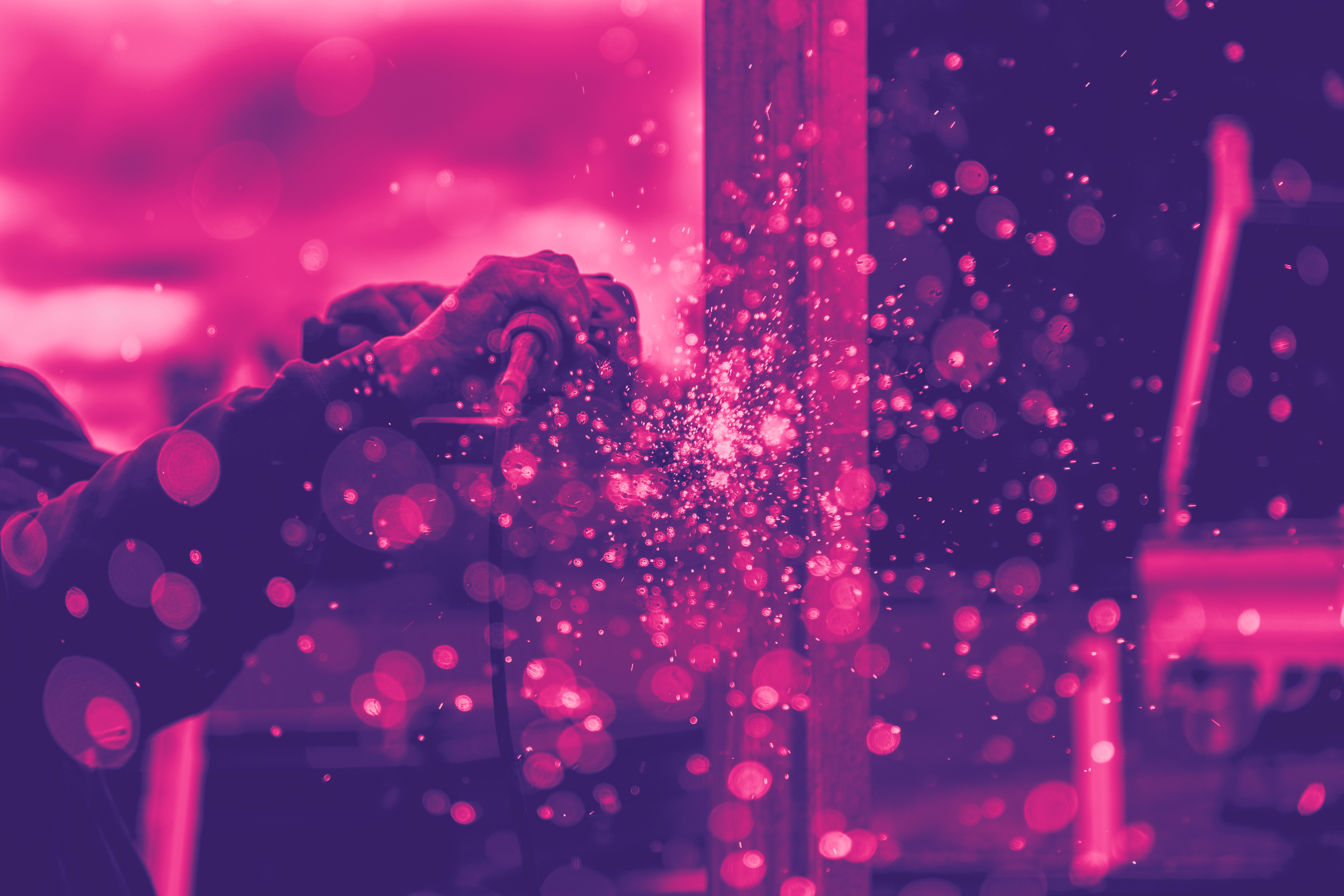 Inzoomad bild på en svetsning där gnistor flyter mot kameran. Med rosa filter