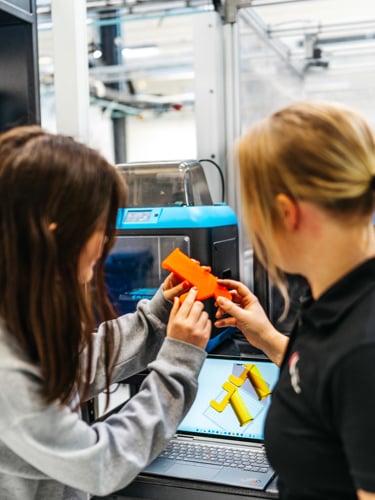 En ung kvinna får handledning av sin kvinnliga handledare vid en maskin med skärm.