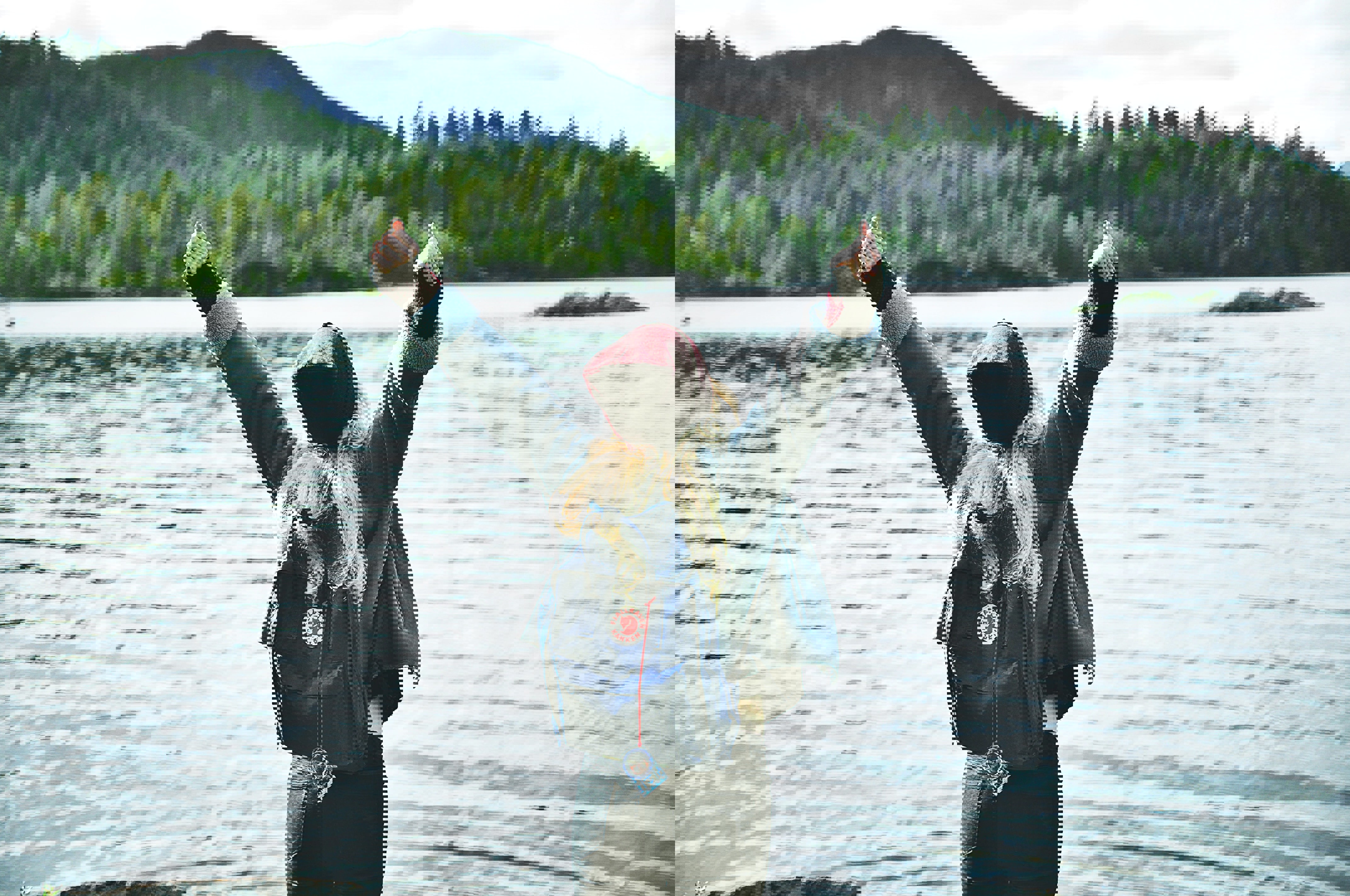 Woman in front of a large lake, with an arctic fox backpack on her back, stretching up her arms