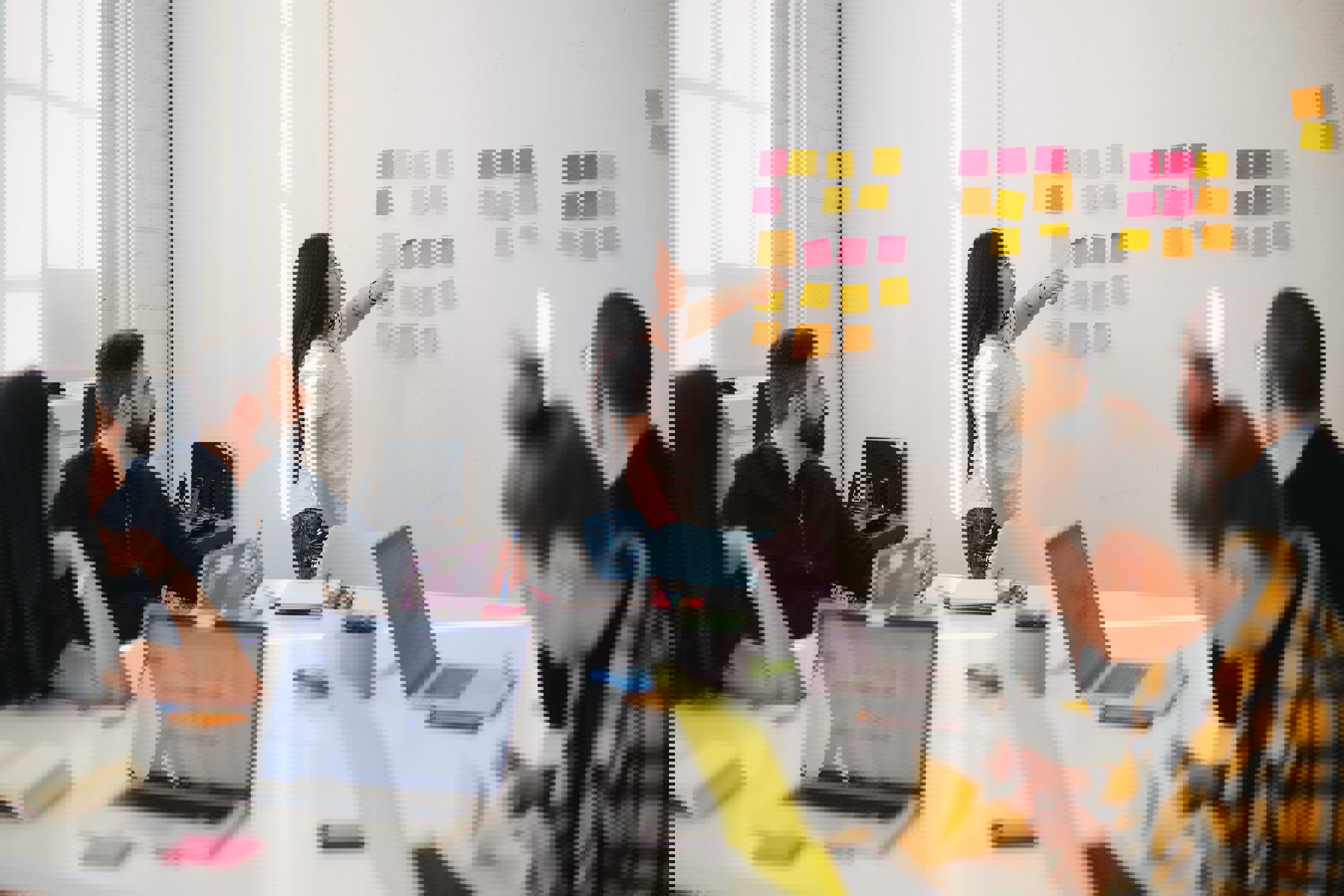 Woman at Whiteboard Covered in Postit Notes Presenting to a Group of People