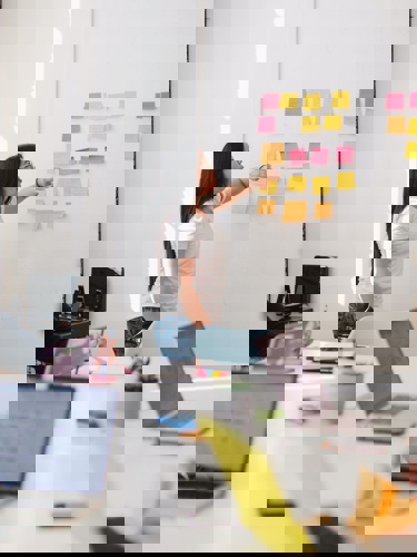 Kvinna vid whiteboard täckt i postitlappar presenterar för en grupp personer